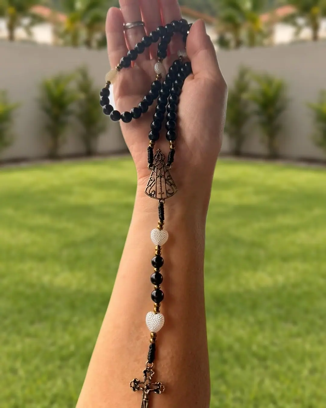 Terço de contas pretas com corações brancos, medalha de Nossa Senhora Aparecida e crucifixo prateado