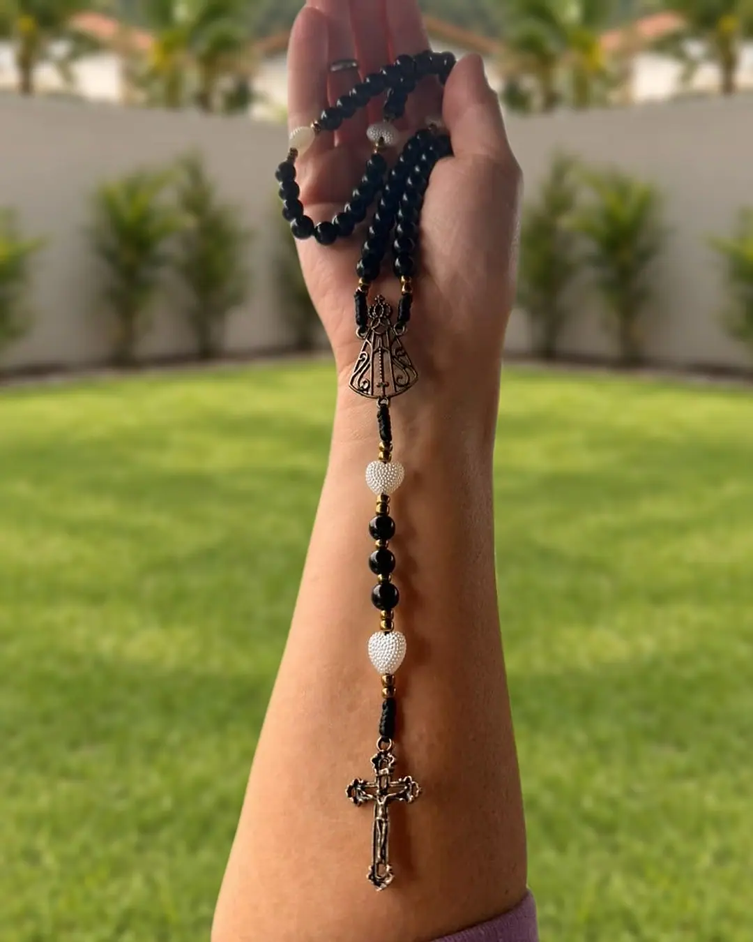 Terço de contas pretas com corações brancos, medalha de Nossa Senhora Aparecida e crucifixo prateado